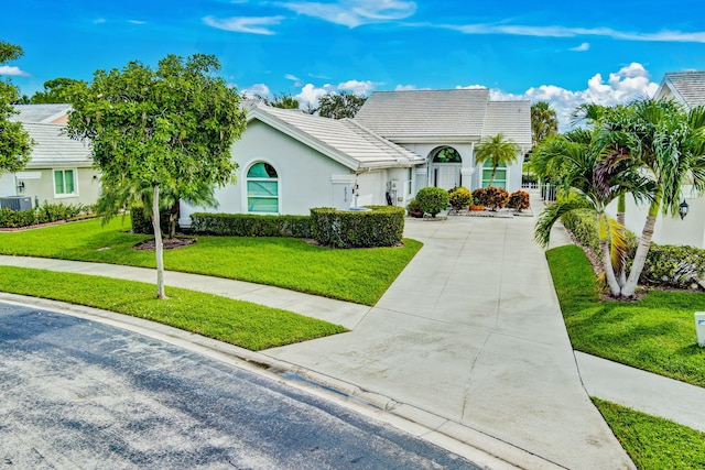 view of front of house with concrete driveway, a tiled roof, a front lawn, and stucco siding