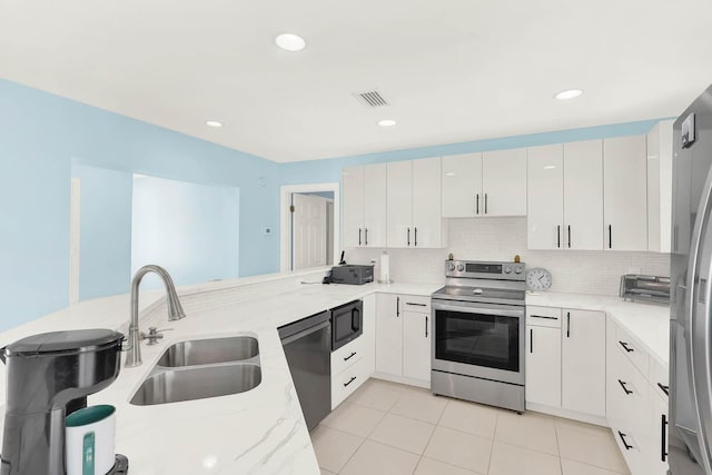 kitchen with light stone counters, tasteful backsplash, appliances with stainless steel finishes, white cabinets, and a peninsula