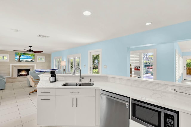 kitchen with a warm lit fireplace, white cabinets, appliances with stainless steel finishes, open floor plan, and a sink