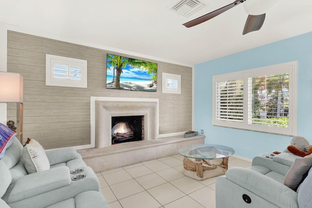 living room featuring a warm lit fireplace, visible vents, ceiling fan, and light tile patterned flooring