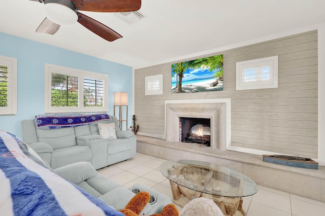 living area featuring ceiling fan, a premium fireplace, light tile patterned flooring, and visible vents