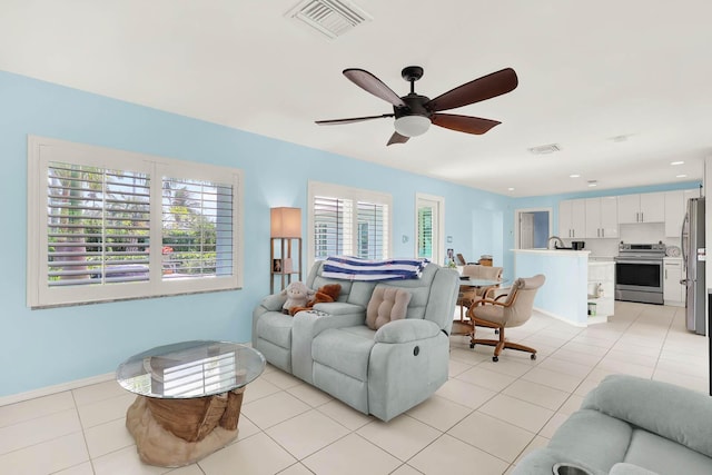 living area with ceiling fan, light tile patterned flooring, visible vents, and baseboards