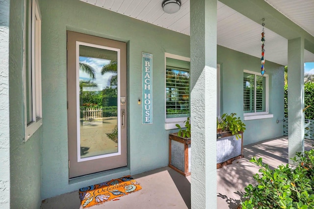 view of exterior entry featuring a porch and stucco siding