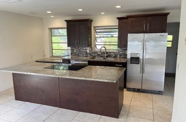 kitchen featuring light stone counters, a sink, stainless steel fridge with ice dispenser, and tasteful backsplash