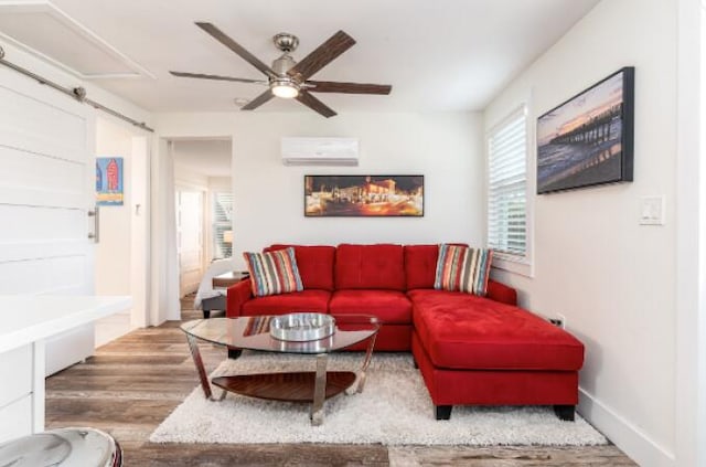 living area featuring light wood finished floors, a barn door, a ceiling fan, a wall mounted AC, and baseboards