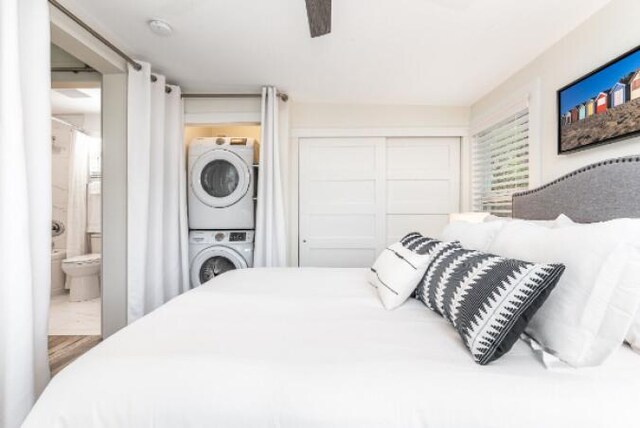 bedroom with a closet, connected bathroom, a ceiling fan, and stacked washer / drying machine