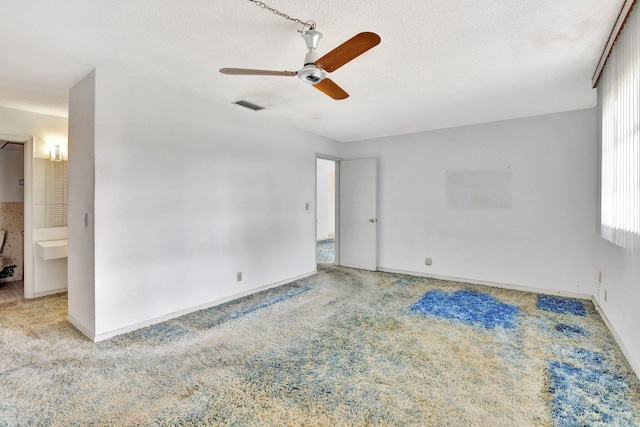 carpeted empty room with a ceiling fan, visible vents, a textured ceiling, and baseboards