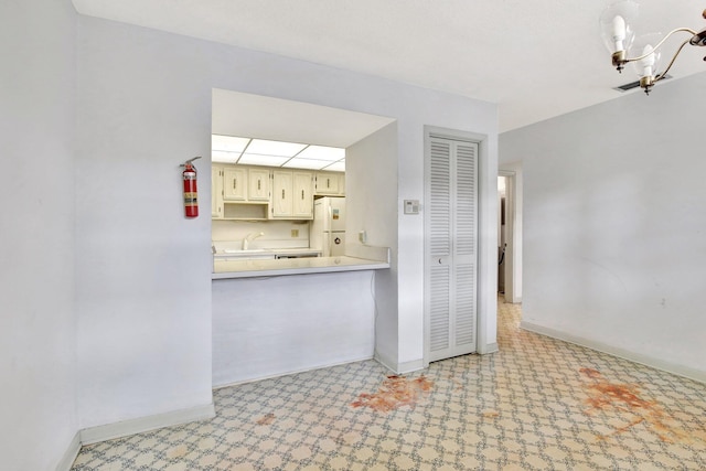 kitchen with a notable chandelier, freestanding refrigerator, a sink, baseboards, and tile patterned floors