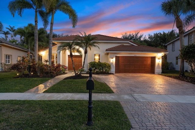 mediterranean / spanish home with a tile roof, an attached garage, decorative driveway, a front lawn, and stucco siding