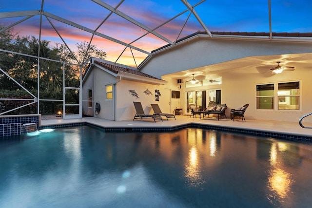 pool at dusk with glass enclosure, a patio area, a ceiling fan, and an outdoor pool