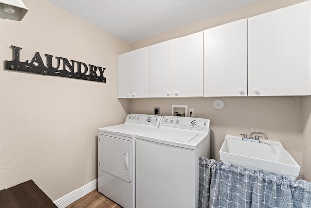 washroom with washing machine and clothes dryer, cabinet space, a sink, wood finished floors, and baseboards