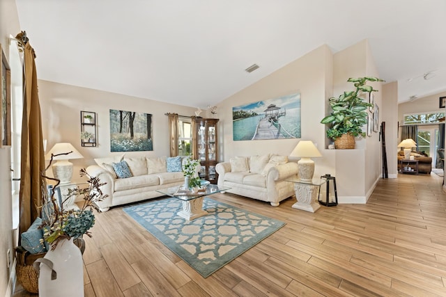 living area featuring lofted ceiling, light wood finished floors, a wealth of natural light, and visible vents