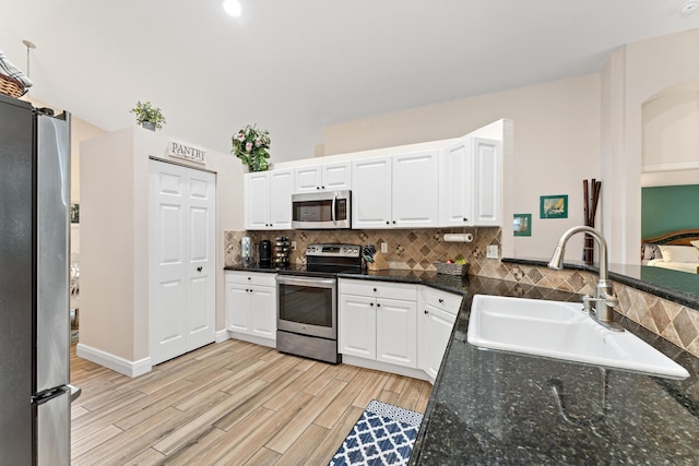 kitchen with backsplash, appliances with stainless steel finishes, white cabinets, a sink, and light wood-type flooring