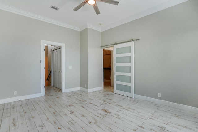 interior space with ceiling fan, a barn door, wood finished floors, visible vents, and ornamental molding