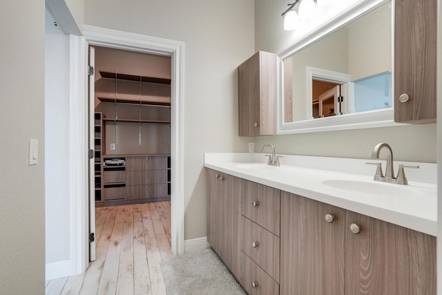 full bath featuring double vanity, a sink, a spacious closet, and wood finished floors