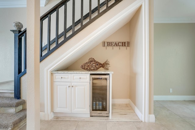 bar featuring light tile patterned flooring, a bar, beverage cooler, baseboards, and stairs