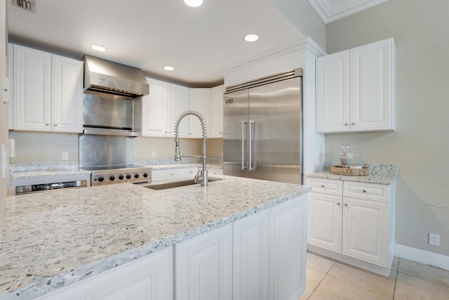 kitchen featuring wall chimney exhaust hood, light stone counters, stainless steel built in refrigerator, white cabinetry, and a sink