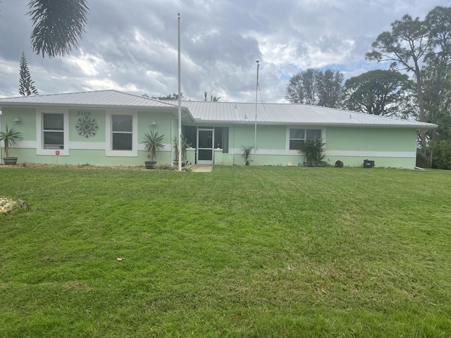 rear view of house with metal roof, a lawn, and stucco siding