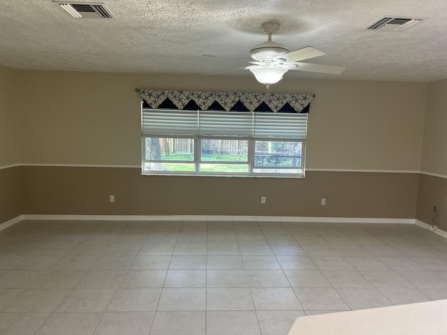 spare room with a textured ceiling, a ceiling fan, visible vents, and baseboards