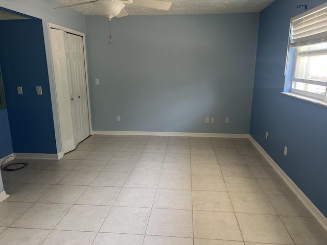 empty room with ceiling fan, light tile patterned floors, baseboards, and a textured ceiling