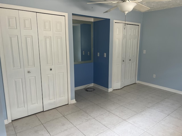 unfurnished bedroom featuring baseboards, multiple closets, light tile patterned floors, a textured ceiling, and a ceiling fan