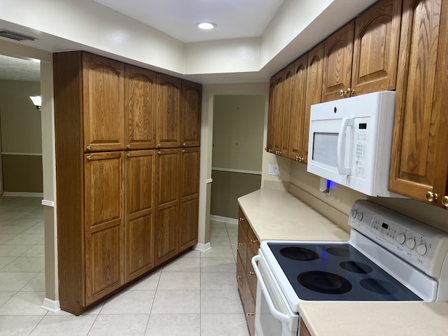 kitchen featuring baseboards, light countertops, light tile patterned floors, brown cabinetry, and white appliances