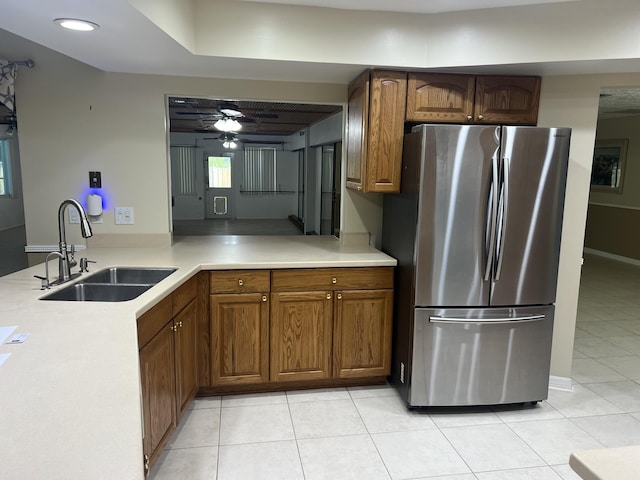 kitchen with a sink, freestanding refrigerator, light tile patterned flooring, brown cabinetry, and light countertops