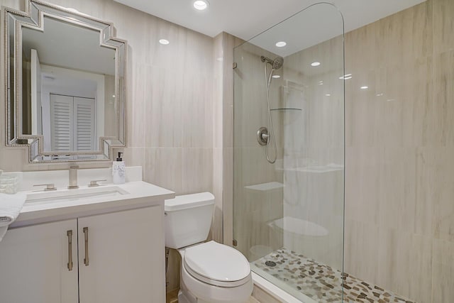 bathroom featuring toilet, vanity, tile walls, a closet, and a tile shower