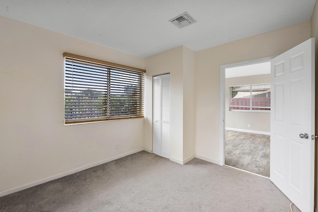 unfurnished bedroom featuring light carpet, a closet, visible vents, and baseboards