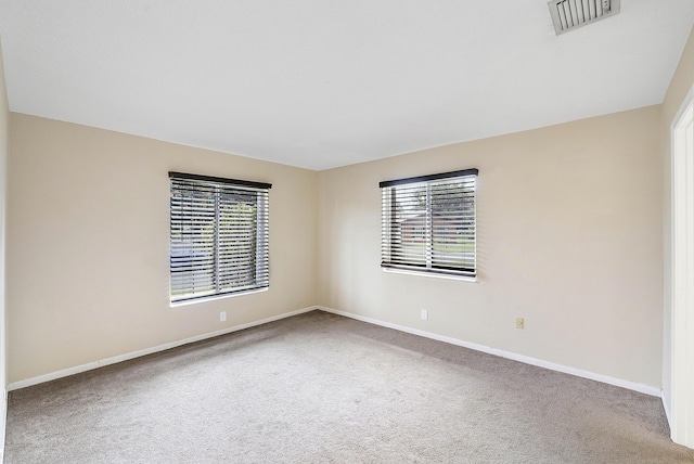 carpeted empty room featuring a healthy amount of sunlight, visible vents, and baseboards