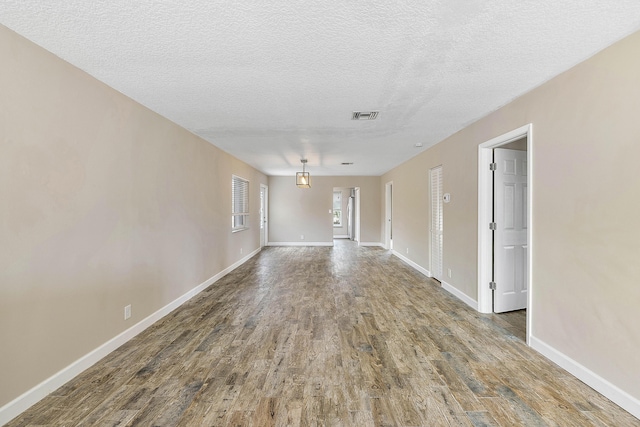 interior space with a textured ceiling, wood finished floors, visible vents, and baseboards