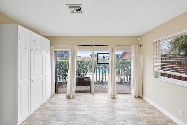 doorway featuring a textured ceiling, light wood-style flooring, visible vents, and a healthy amount of sunlight