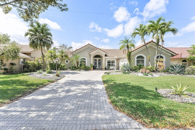 mediterranean / spanish home featuring a garage, a front yard, decorative driveway, and stucco siding