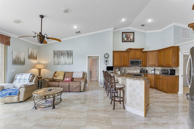 kitchen with stainless steel microwave, visible vents, brown cabinetry, open floor plan, and a kitchen bar