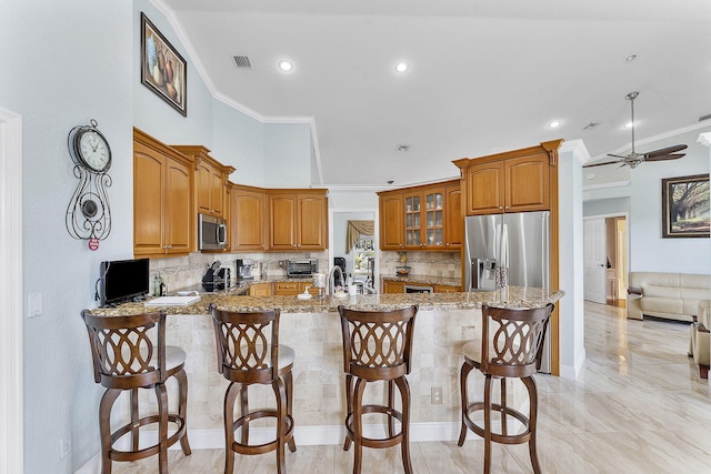 kitchen featuring appliances with stainless steel finishes, brown cabinets, light stone counters, ornamental molding, and a peninsula