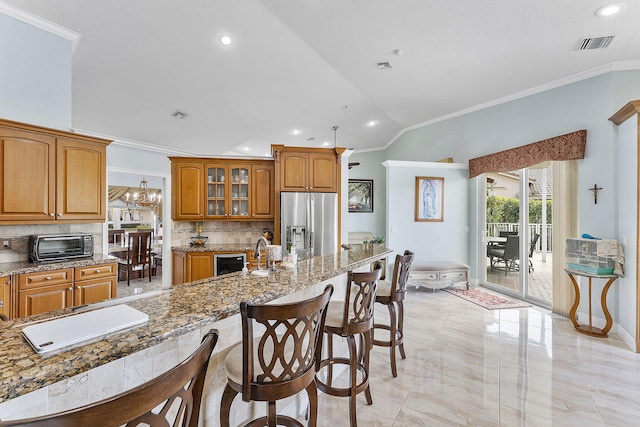 kitchen featuring visible vents, brown cabinetry, stainless steel fridge with ice dispenser, a breakfast bar, and light stone countertops