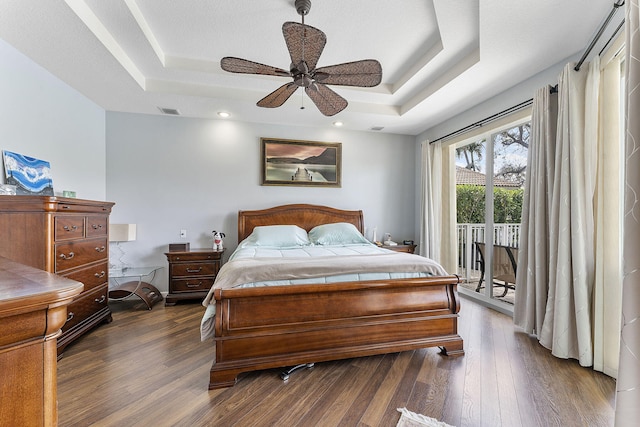 bedroom featuring dark wood-style floors, a tray ceiling, visible vents, and access to exterior