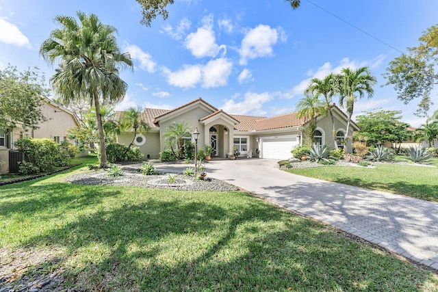 mediterranean / spanish-style house with a tile roof, an attached garage, decorative driveway, a front lawn, and stucco siding