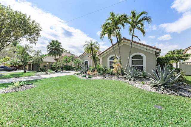 mediterranean / spanish house with driveway, stucco siding, a tile roof, and a front yard