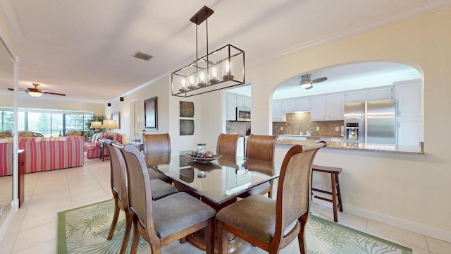 dining space featuring light tile patterned floors, ceiling fan, arched walkways, visible vents, and crown molding