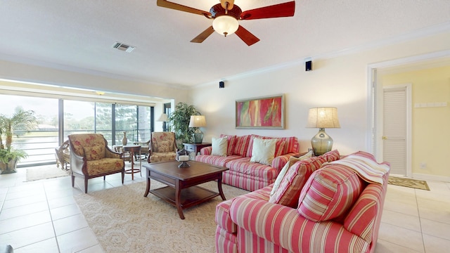 living area with light tile patterned floors, visible vents, baseboards, a ceiling fan, and ornamental molding