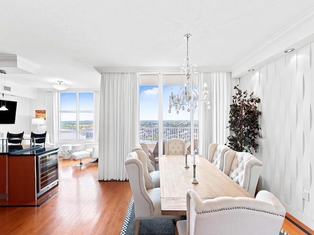 dining space with wine cooler, a notable chandelier, visible vents, ornamental molding, and light wood finished floors