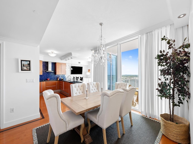 dining space featuring baseboards, crown molding, light wood-type flooring, and a notable chandelier