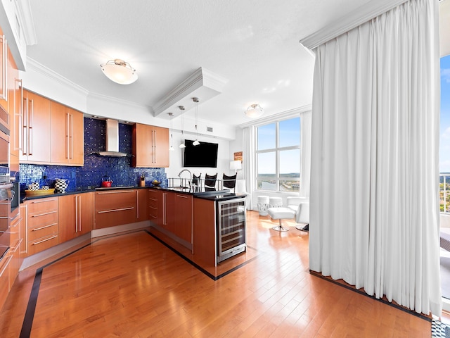 kitchen with wine cooler, a peninsula, wall chimney exhaust hood, dark countertops, and decorative light fixtures