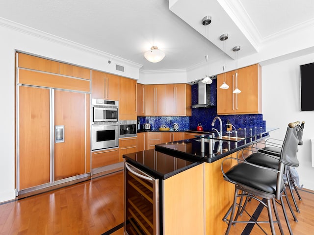 kitchen featuring dark countertops, hanging light fixtures, paneled built in fridge, wall chimney range hood, and beverage cooler