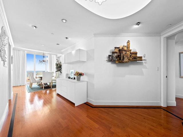 unfurnished living room with light wood finished floors, baseboards, crown molding, and an inviting chandelier