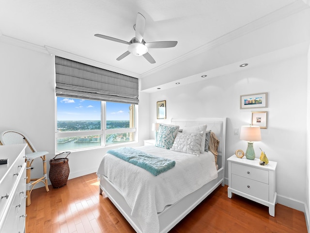 bedroom featuring wood-type flooring, a water view, crown molding, and baseboards