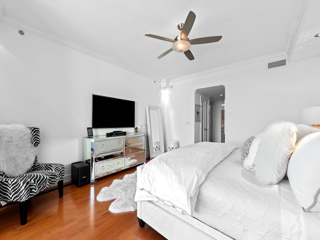 bedroom with ornamental molding, a ceiling fan, visible vents, and wood finished floors