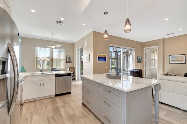 kitchen featuring appliances with stainless steel finishes, decorative light fixtures, light stone countertops, white cabinetry, and a sink