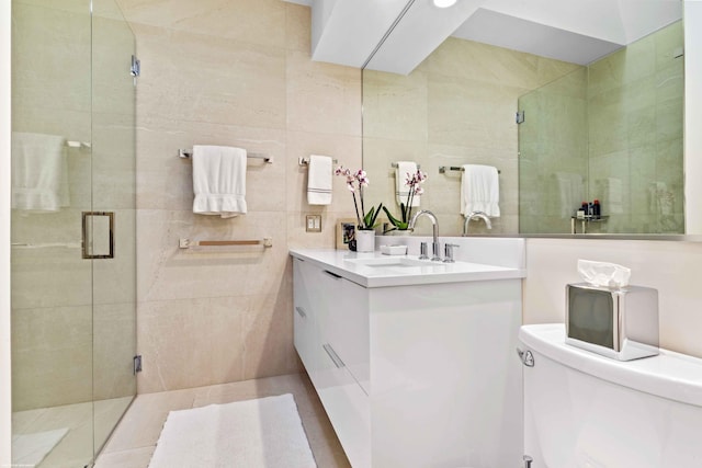 bathroom featuring toilet, a stall shower, vanity, and tile walls